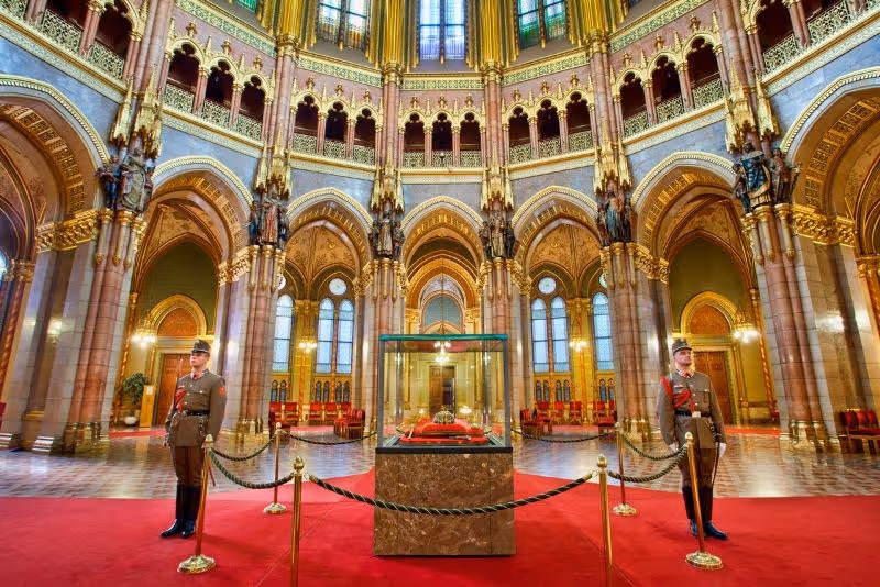 The opulent Council Hall inside the Hungarian Parliament Building, with red carpets and ornate gold decorations.
