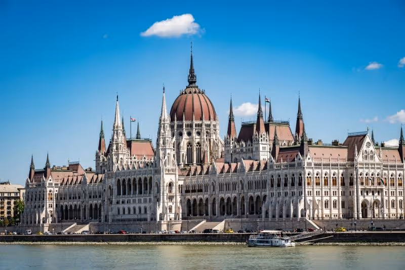The opulent Council Hall inside the Hungarian Parliament Building, with red carpets and ornate gold decorations.